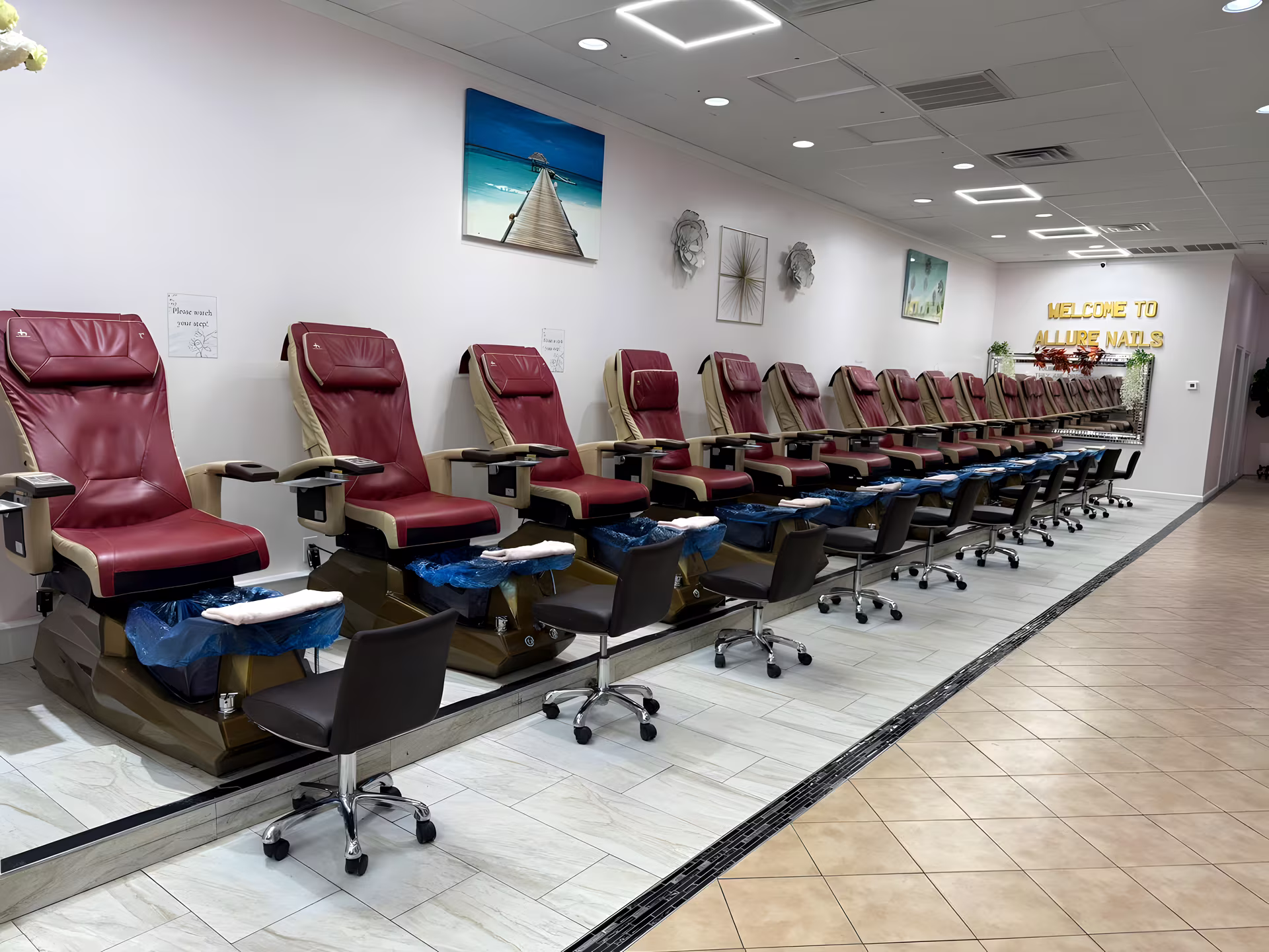 Row of red leather spa pedicure chairs under the Welcome to Allure Nails sign